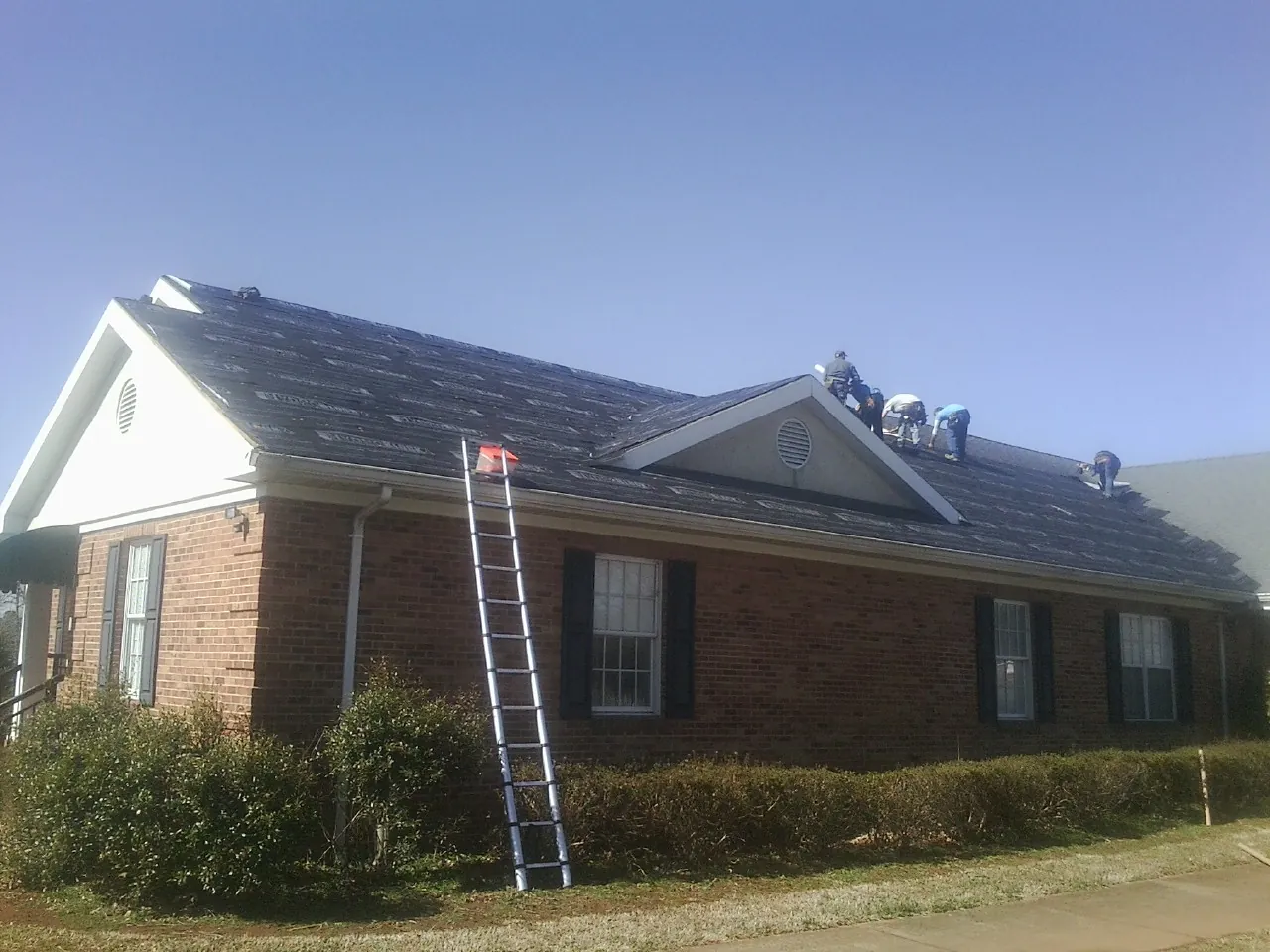 Crew tearing shingles off a brick ranch roof with a ladder set — Emergency Roof Repair work by our crew in Fond Du Lac