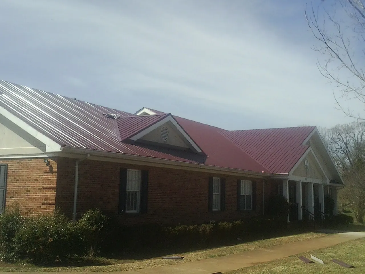 Red metal roof with gabled entries on a long brick building, from a Hail Damage Roof Repair job in Fond Du Lac