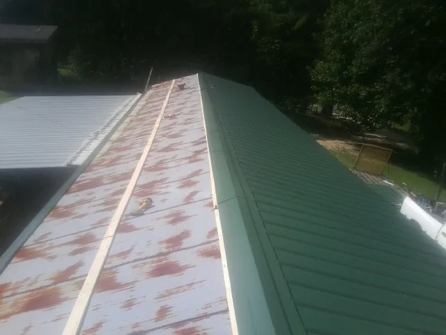 Old rusted panels beside newly installed green metal roofing — Wind Damage Roof Repair by Roofing Brothers in Fond Du Lac