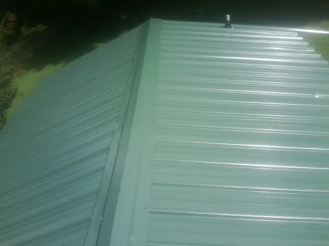New green metal panels meeting at the ridge of a roof — Flat Roof Repair work by our crew in Fond Du Lac
