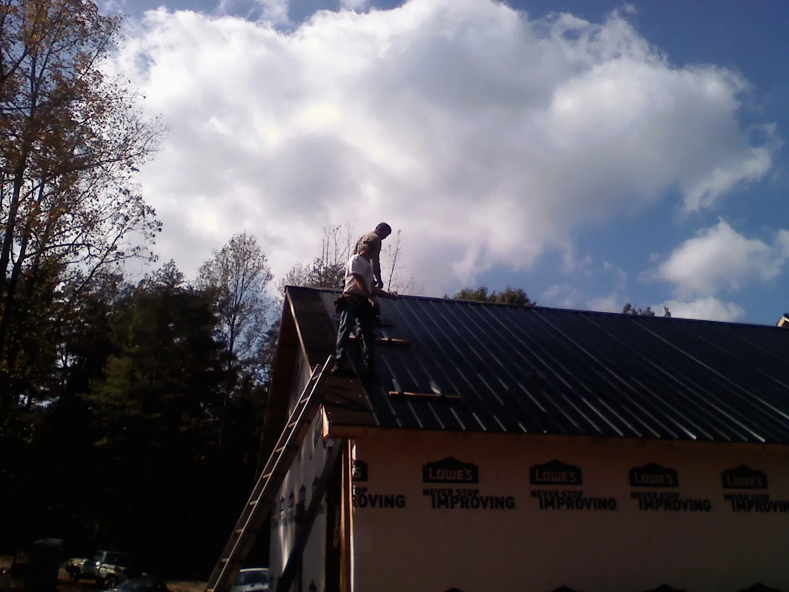 Roofer fastening dark metal panels high against a cloudy sky, from a Roof Inspection job in Fond Du Lac