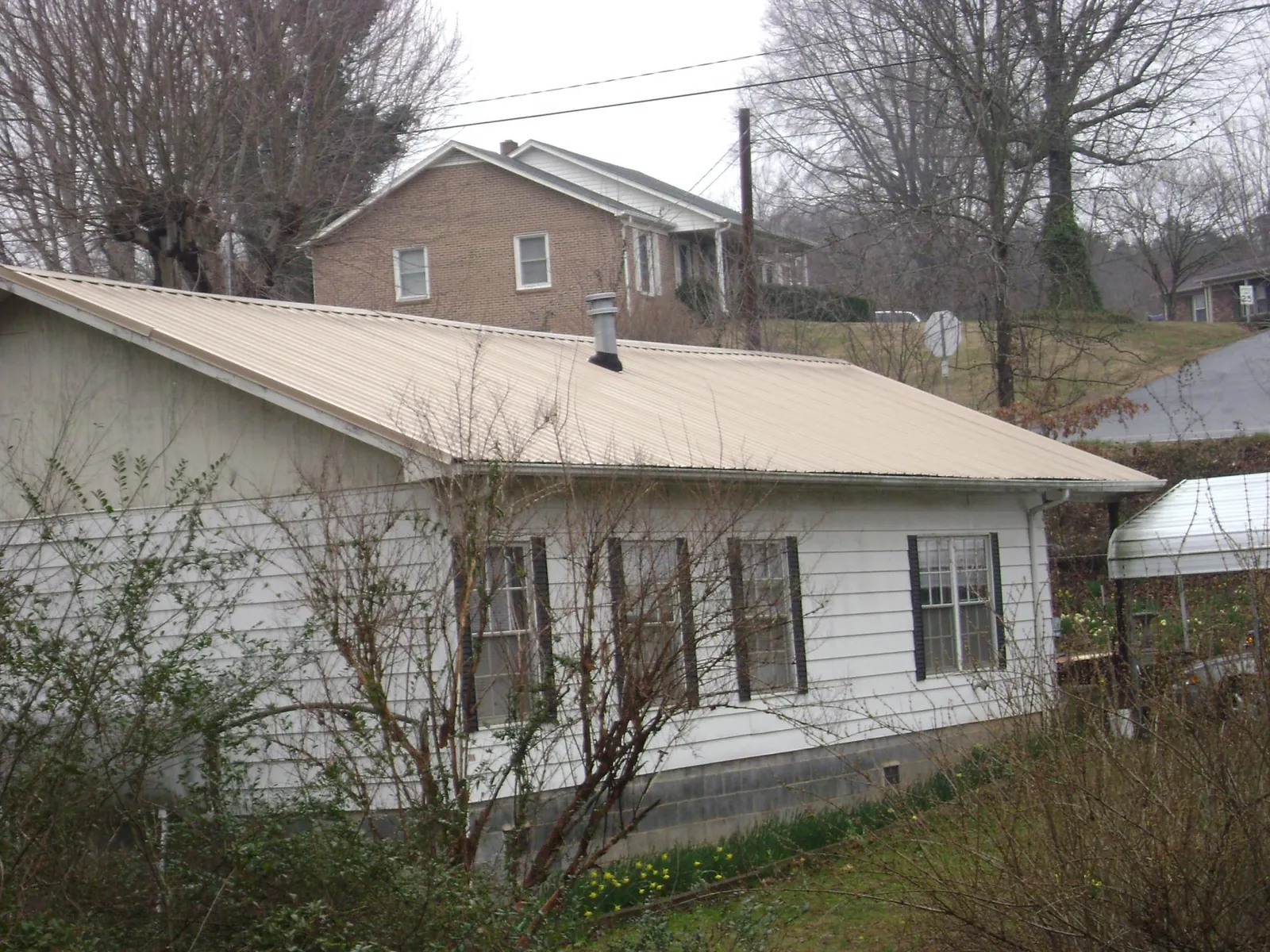 Tan metal roof on a white sided house set into a hillside — Commercial Roofing by Roofing Brothers in Fond Du Lac