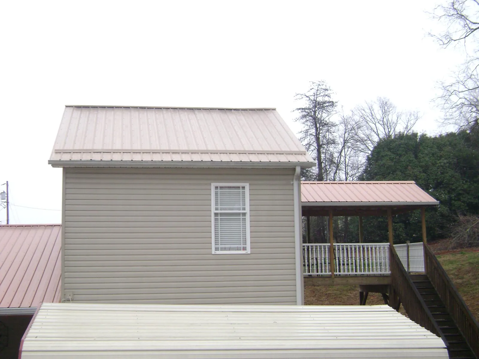 Tan metal roofs on a two story addition and attached porch, from a Roof Replacement job in Fond Du Lac